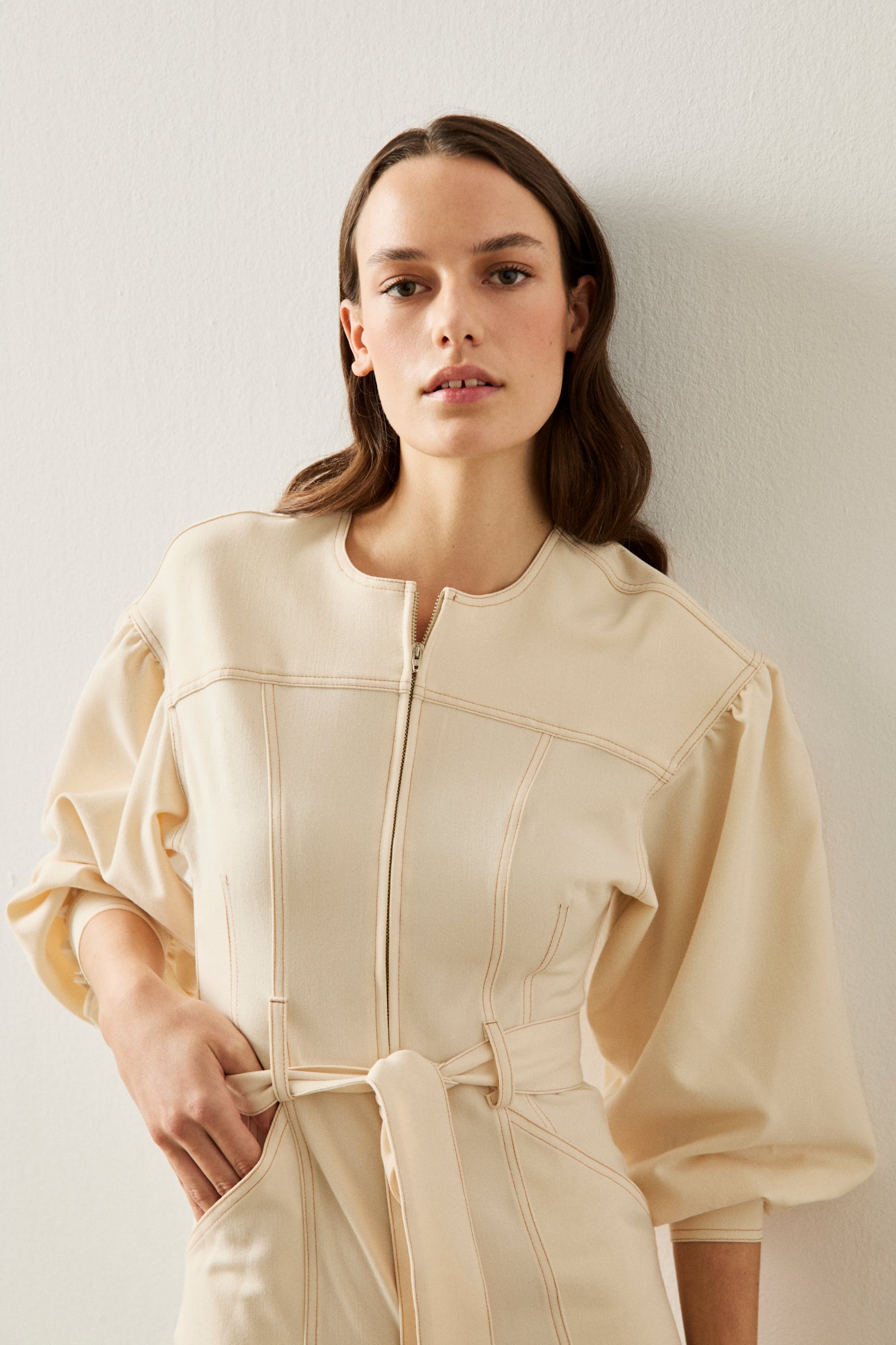 Mono color crema con manga abullonada, detalle de costuras y cremallera delantera