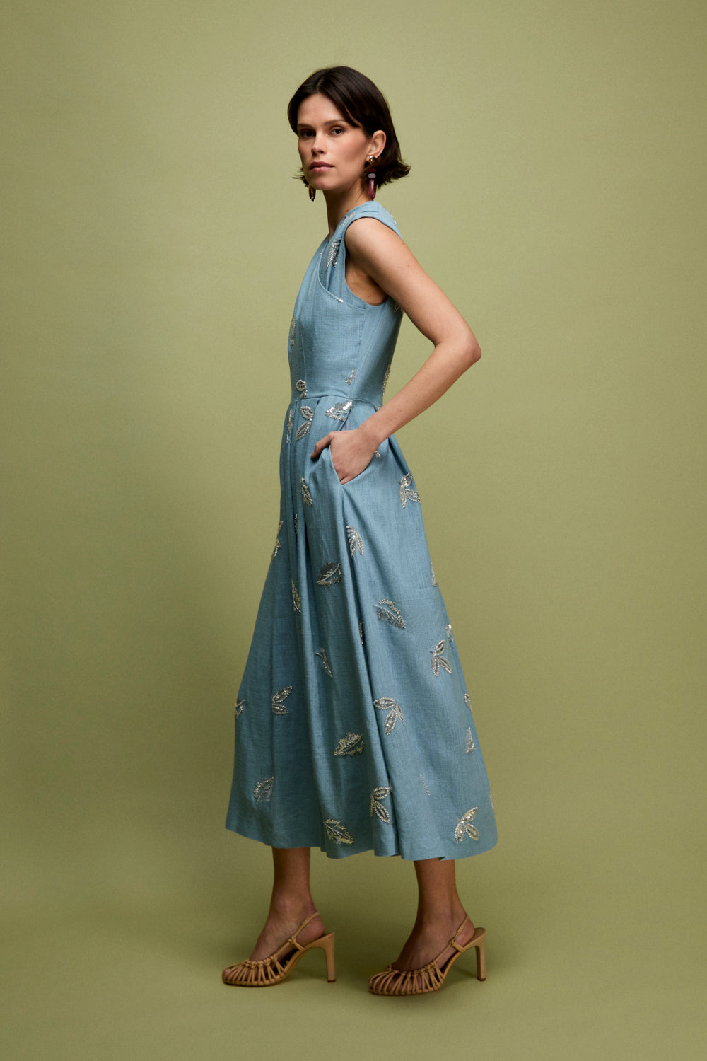 Vestido midi en color celeste con bordados de pailletes. Este vestido tiene pieza fruncida superpuesta en pecho y corte en la cintura. La falda está tableada e incluye bolsillos.