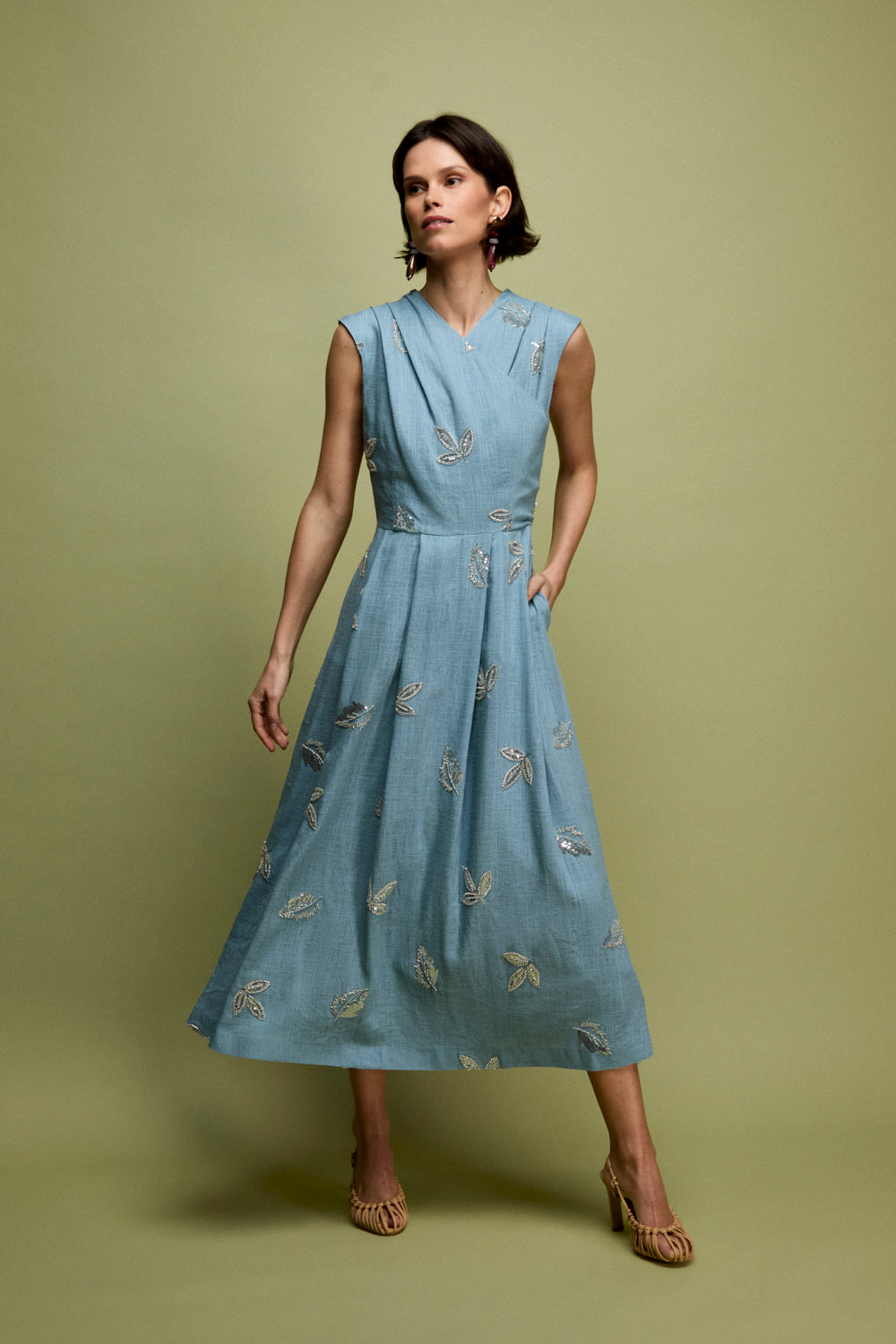 Vestido midi en color celeste con bordados de pailletes. Este vestido tiene pieza fruncida superpuesta en pecho y corte en la cintura. La falda está tableada e incluye bolsillos.