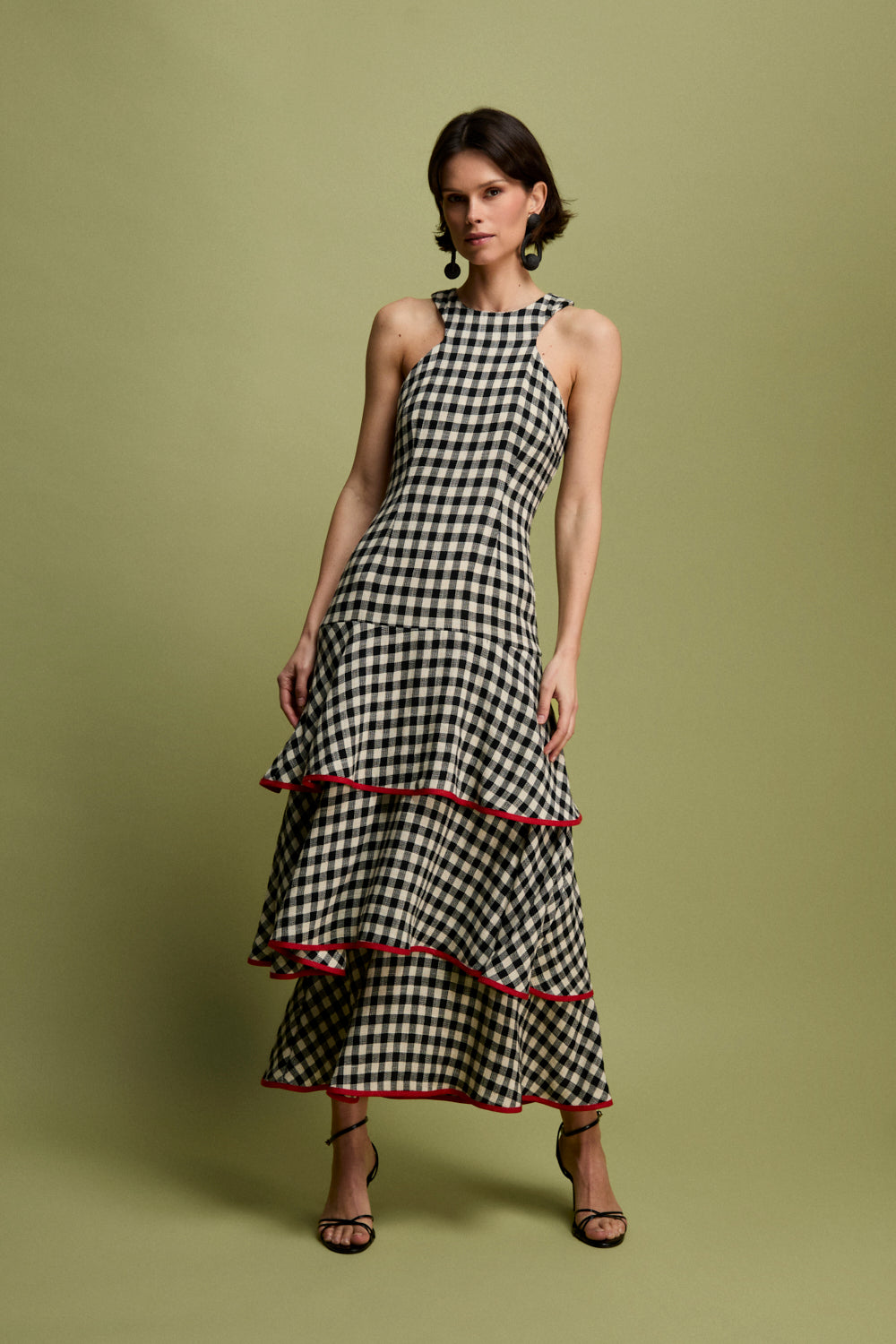 Vestido midi vichy con escote halter y corte en la cintura. La falda está compuesta por volantes viveados en rojo. 